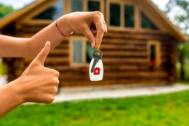 Holding house key with wooden cottage on background - Photo, Image