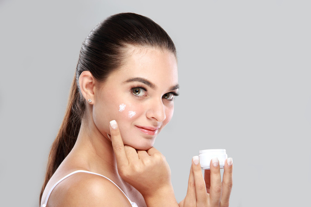 beautiful young woman applying some facial cream on her cheek - Foto, afbeelding