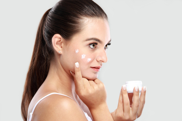 beautiful young woman applying some facial cream on her cheek - Photo, Image
