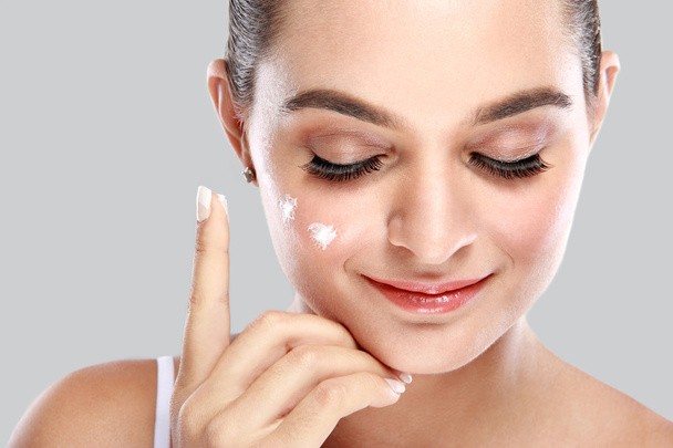 beautiful young woman applying some facial cream on her cheek - 写真・画像