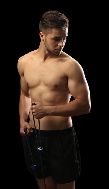 Muscle young man exercising with resistance band on dark background - Фото, изображение