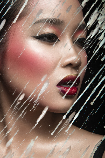 Beautiful Asian girl with bright make-up behind glass and drops of wax. Beauty face.  - Fotoğraf, Görsel