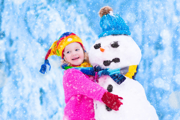 小さな女の子が雪だるまで遊んで - 写真・画像