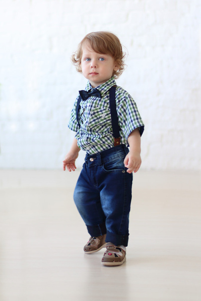 Little handsome curly boy in jeans stands in room - Photo, image