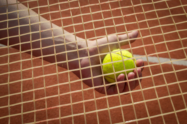 Mano sosteniendo pelota de tenis a través de la raqueta
 - Foto, Imagen
