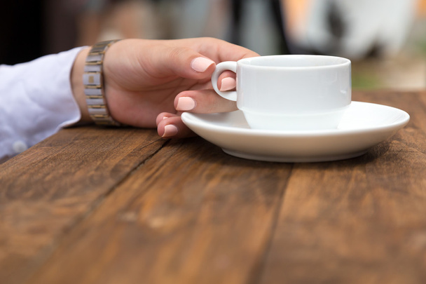 Female hand holding white coffee mug at grunge wood desk - Foto, Imagem
