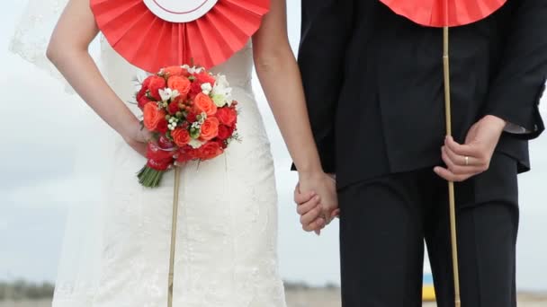 Η νύφη και ο γαμπρός πίσω θέα κρατώντας στα χέρια τους κόκκινα λουλούδια - Πλάνα, βίντεο