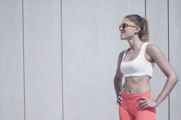 Fit Woman in Fitness Attire Standing Against Wall - Photo, Image