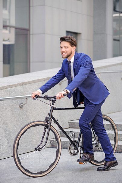 Pleasant businessman standing with bicycle  - 写真・画像