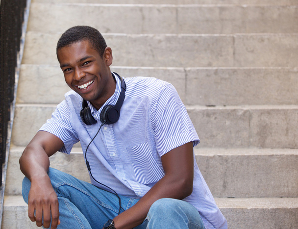 Usměvavý chlapík sedí na schodech vně se sluchátky - Fotografie, Obrázek