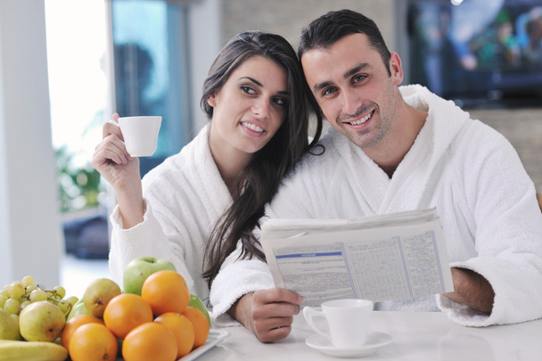 Happy couple reading the newspaper in the kitchen at breakfast - Photo, image
