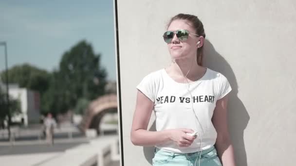 Portret van een grappig jonge meisje op strand luisteren naar muziek in oortelefoons van slimme telefoon mp3-speler. in de stad - Video