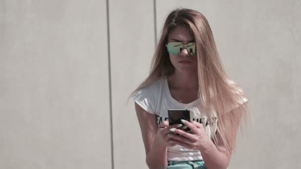 hallgató napszemüveget visel, és a mobiltelefon használata egy szöveges üzenetet, vagy böngésszen online - Felvétel, videó