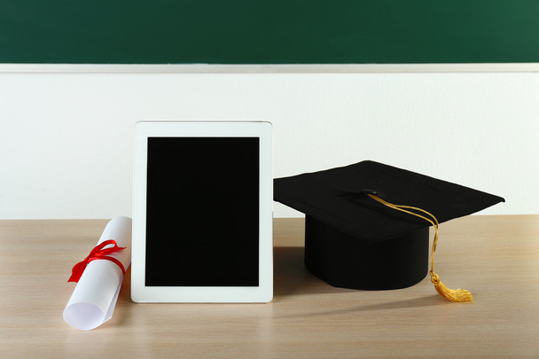 afstuderen cap met Tablet PC- en diploma op tafel in de klas - Foto, afbeelding