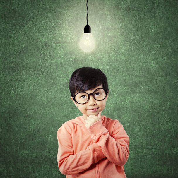 Kid in thinking poses while looking at light bulb - 写真・画像