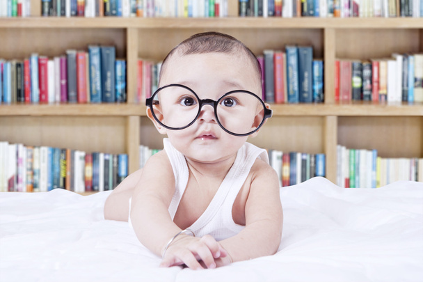 Sweet baby with glasses and a bookcase background - Photo, Image