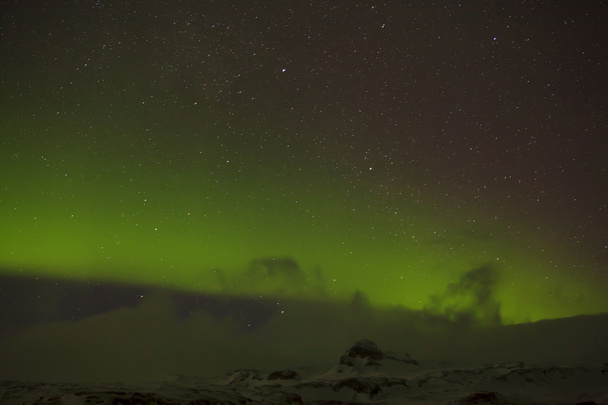 Luces boreales con montañas nevadas en primer plano
 - Foto, Imagen