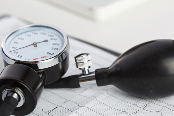 медицинский манометр, лежащий на кардиограмме крупным планом
 - Фото, изображение