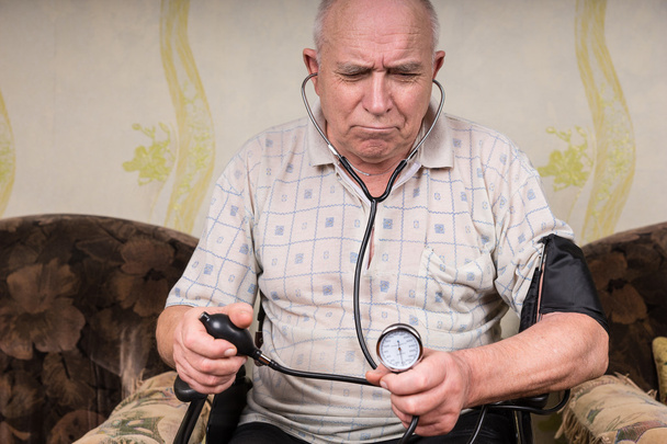 Frowning senior man monitoring his blood pressure - Valokuva, kuva