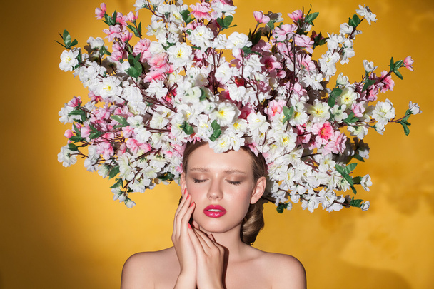 Sensual girl posing in studio looking down. Young model with bouquet of flowers on her head. - 写真・画像