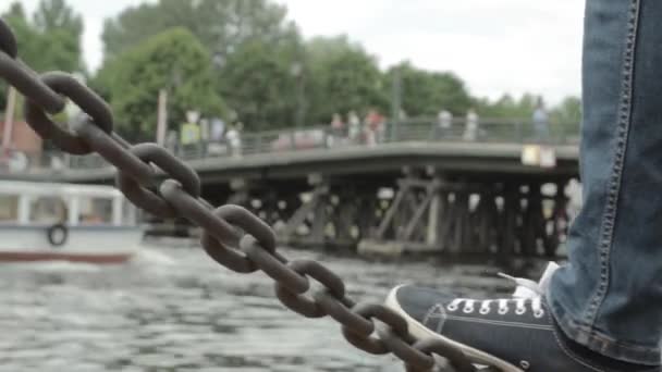 Miesten jalka heiluttaa ketjua sillalla
 - Materiaali, video
