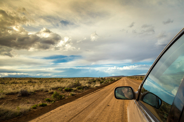 Sonriente hombre conduciendo por el desierto en el camino de tierra
 - Foto, Imagen