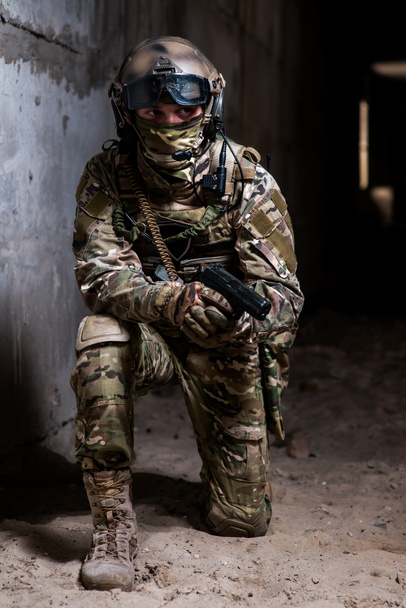 Militaire man in camouflage met een pistool staande knie in het gebouw en controleert het doel - Foto, afbeelding