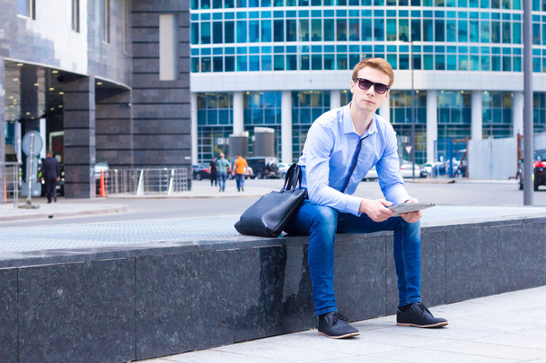 Young businessman sitting in the street near the business center and the works on the tablet - Foto, Imagem