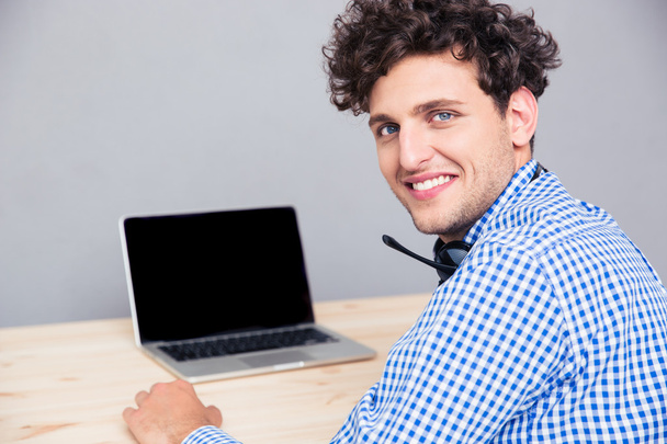 Усміхнений чоловік сидить за столом з ноутбуком
  - Фото, зображення