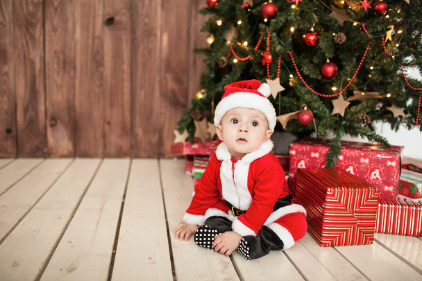Baby in santa suit with gifts near xmas tree - 写真・画像