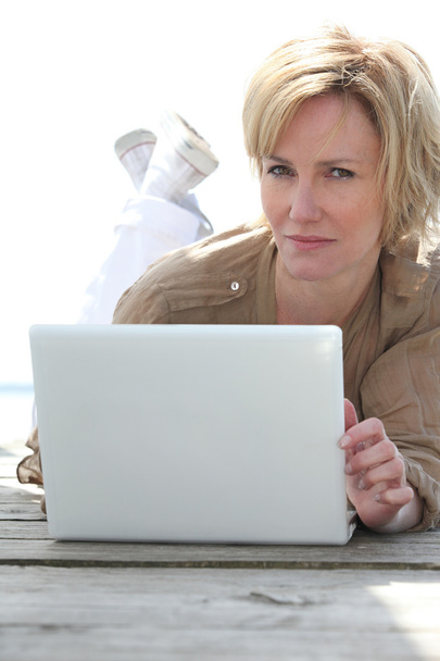 Nainen noudattaen puinen terassi kannettavan tietokoneen
 - Valokuva, kuva