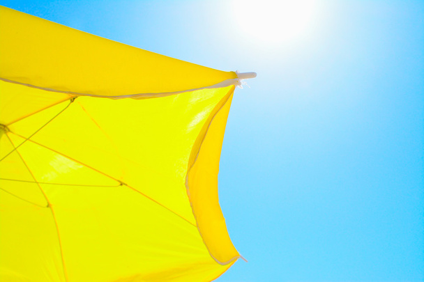 keltainen päivänvarjo paistavan auringon alla
 - Valokuva, kuva