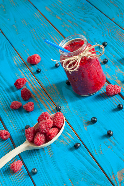 Mason jar with raspberry jam or marmalade and fresh raspberries, blueberries on a rustic wooden table. Cooking background, unique perspective - Fotó, kép
