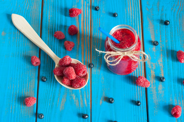 Mason jar with raspberry jam or marmalade and fresh raspberries, blueberries on a rustic wooden table. Cooking background, unique perspective - Photo, Image