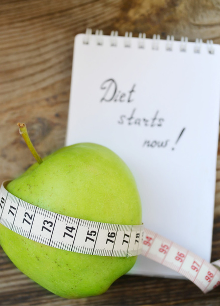 Conceito de dieta com maçã verde, um caderno e uma fita métrica na mesa de madeira
 - Foto, Imagem