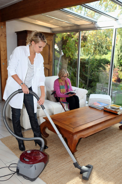 Girl vacuuming for an elderly woman - Фото, зображення
