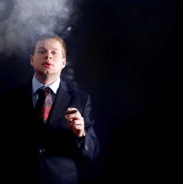 O homem mascarado fuma um charuto, olha para nós. Muita fumaça. Um fundo escuro
 - Foto, Imagem