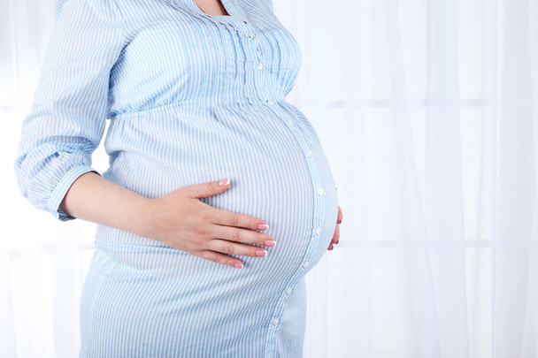 Beautiful young pregnant woman touching her belly on light background - Fotoğraf, Görsel