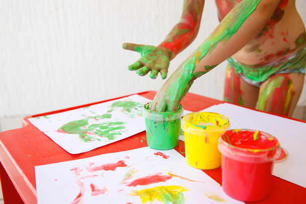 Дитина занурює пальці в фарби для миття пальців
 - Фото, зображення