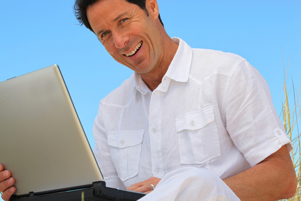 Man smiling on laptop in blue sky - Foto, immagini