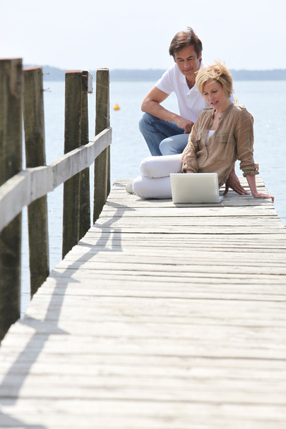 Mature couple with laptop seated on pontoon - Foto, Imagen