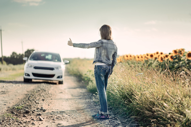Κορίτσι που παρουσιάζει τους αντίχειρες μέχρι ένα αυτοκίνητο, περνώντας το δρόμο - Φωτογραφία, εικόνα