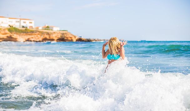 beautiful young blonde woman jumping big waves in sea - Photo, image