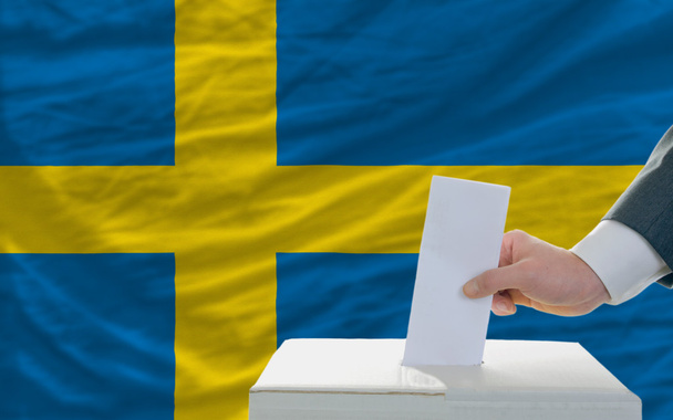 Homem votando nas eleições na Suécia em frente à bandeira
 - Foto, Imagem