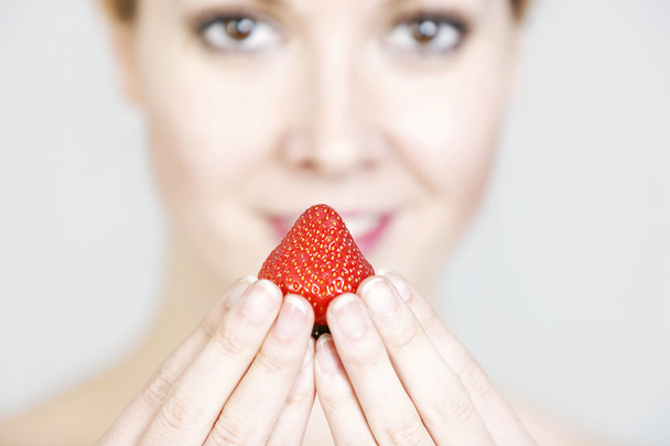 Woman holding up a strawberry - Foto, Imagen