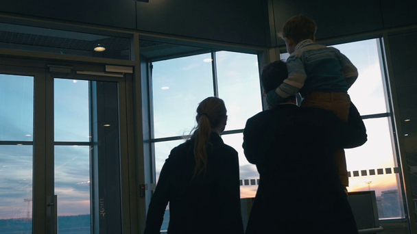 Молодая семья смотрит в окно аэропорта на закате
 - Кадры, видео