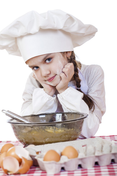 Little girl in a white apron and chefs hat knead the dough in th - Фото, изображение