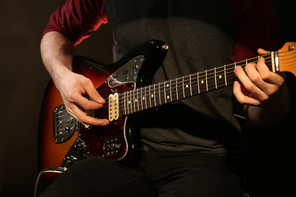 νεαρός άνδρας παίζει στην ηλεκτρική κιθάρα σε σκούρο φόντο - Φωτογραφία, εικόνα
