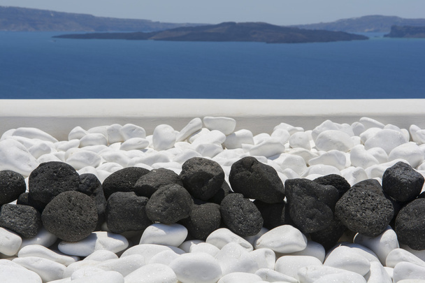 Czarne kamienie wulkaniczne nad białym. Szczegóły dekoracji na wyspie Santorini - Zdjęcie, obraz