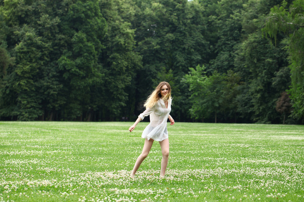 Young beautiful girl in the white shirt is running on the green  - Fotografie, Obrázek